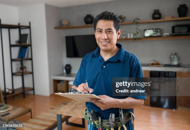 happy electrician working at a house and smiling while writing on a clipboard - plumber home stock pictures, royalty-free photos & images