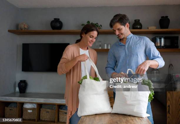 happy couple arriving home with the groceries using reusable bags - reusable bag isolated stock pictures, royalty-free photos & images