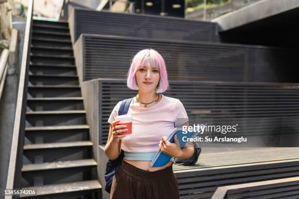 image of young woman with colorful hair on university campus and holding sustainable coffee cup - americana rosa imagens e fotografias de stock