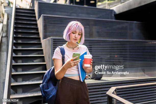 young woman with colorful hair holding coffee in cardboard cup and using her smart phone - pink hair stock pictures, royalty-free photos & images