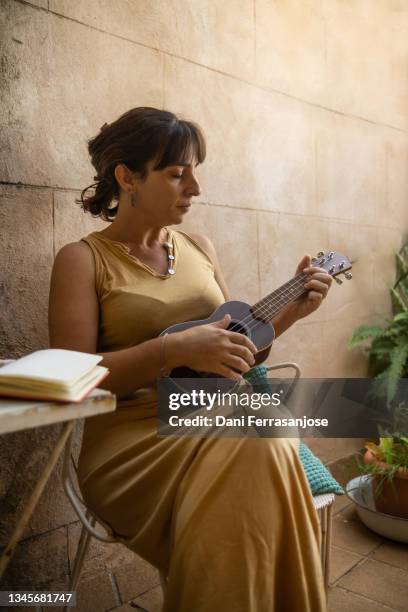 online music student practices with her ukulele after work to learn how to make something of her life. - ukelele stock pictures, royalty-free photos & images