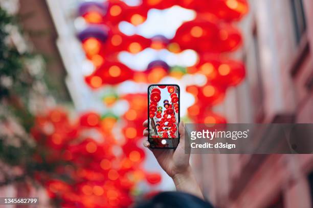 cropped shot of young asian woman taking photos of traditional chinese red lanterns with smartphone hanging along the city street. traditional chinese culture, festival and celebration event theme - festival de las linternas chino fotografías e imágenes de stock