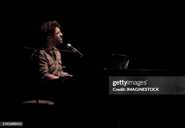 man singing while playing the piano in a darkened room - keyboard white stockfoto's en -beelden