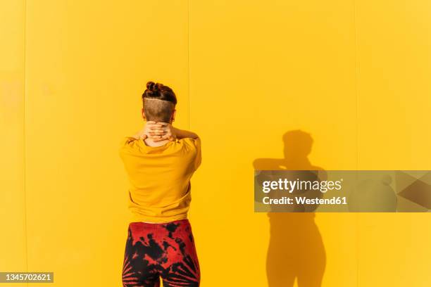 woman with hands on neck standing in front of yellow wall - androgynous stock pictures, royalty-free photos & images