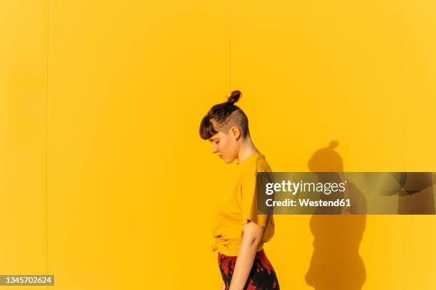 androgynous person with half-shaved hairstyle standing by yellow wall - androgynous stock pictures, royalty-free photos & images