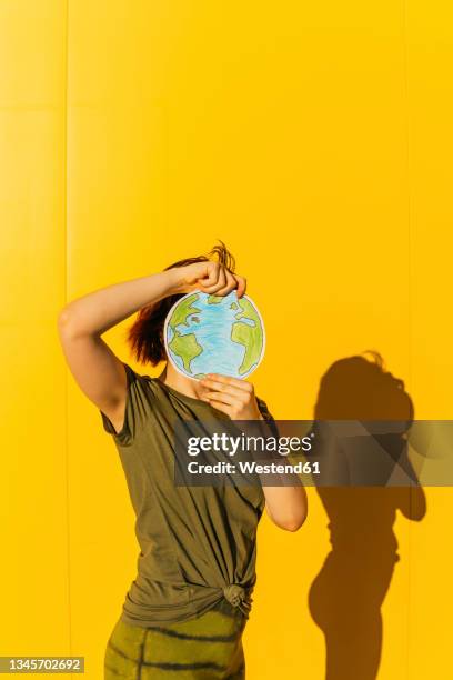 woman holding planet earth paper in front of yellow wall - 両性具有点のイラスト素材／クリップアート素材／マンガ素材／アイコン素材