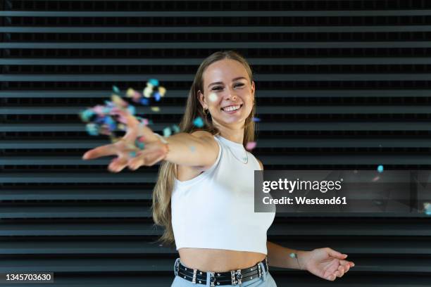 happy female freelancer throwing confetti while standing in front of wall - werfen stock-fotos und bilder