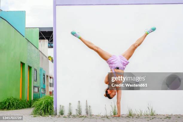 woman talking on mobile phone while doing handstand in front of wall - handstand stock pictures, royalty-free photos & images