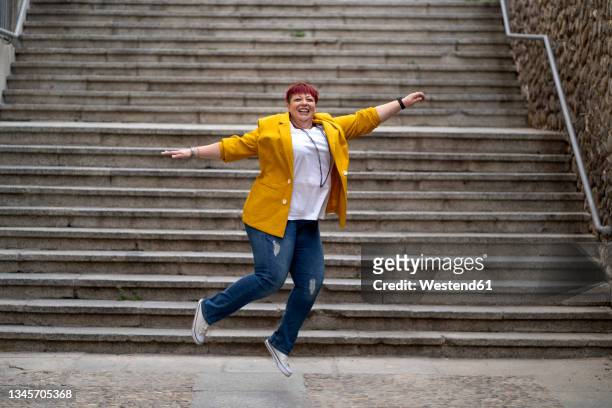 carefree mature woman jumping in front of steps - arms outstretched full body stock pictures, royalty-free photos & images