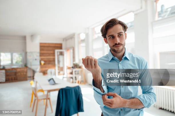 businessman unbuttoning sleeve while standing in office - abrochar fotografías e imágenes de stock