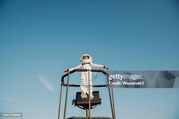 boy wearing space suit standing with arms outstretched on chair - space helmet stock pictures, royalty-free photos & images