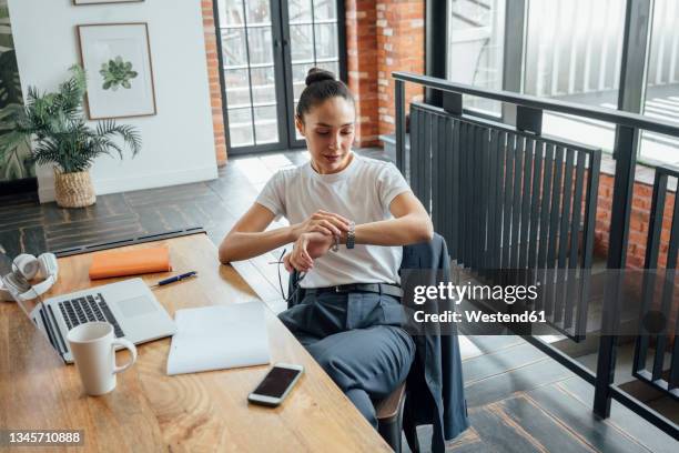businesswoman checking time on wristwatch in office - tijdstip stockfoto's en -beelden