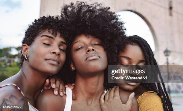 young women with eyes closed leaning on shoulder's of female friend - african woman hair stock-fotos und bilder