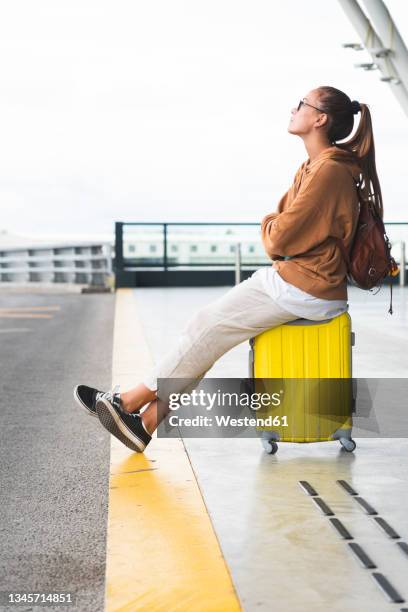 woman sitting on luggage at airport - luggage trolley stock-fotos und bilder