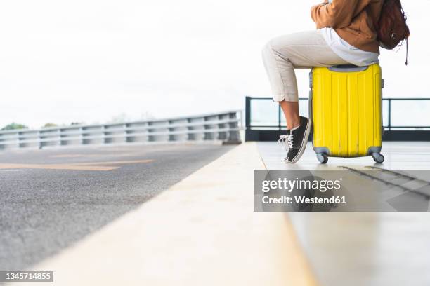 woman sitting on wheeled luggage at airport - yellow suitcase stock pictures, royalty-free photos & images