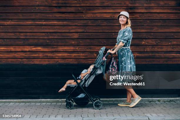 mid adult woman pushing baby stroller on footpath - cochecito de bebé fotografías e imágenes de stock