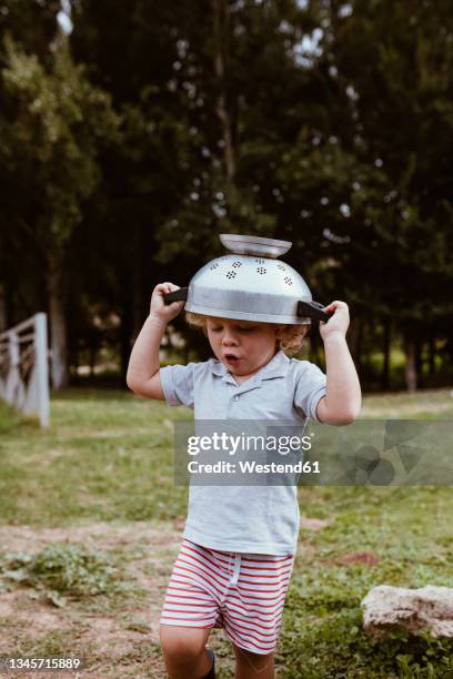 boy wearing colander on head while playing on meadow - colander 個照片及圖片檔