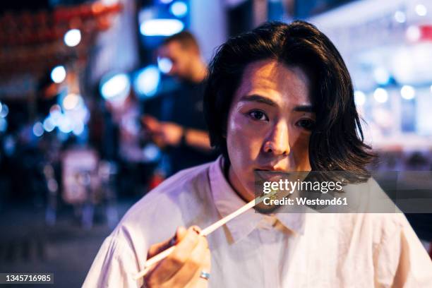 young man eating food with chopsticks at night - asian man long hair stock pictures, royalty-free photos & images