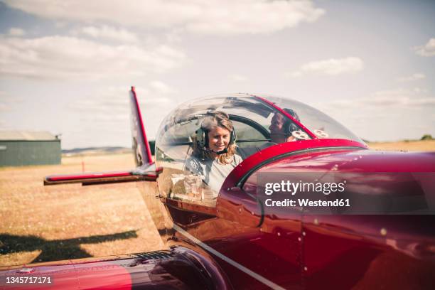 smiling mature woman piloting airplane during sunny day - female pilot stock-fotos und bilder