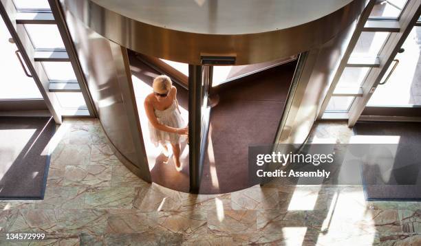 woman in sun dress walks into hotel lobby. - revolving door foto e immagini stock