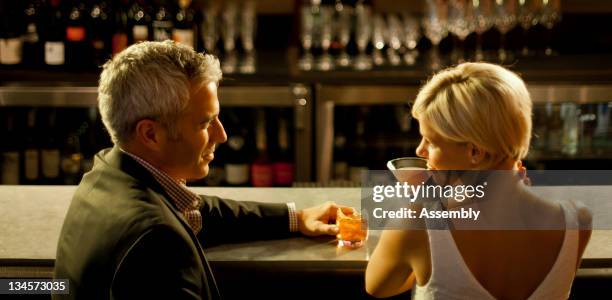 a couple sits with their drinks at a bar. - couple bar stock pictures, royalty-free photos & images