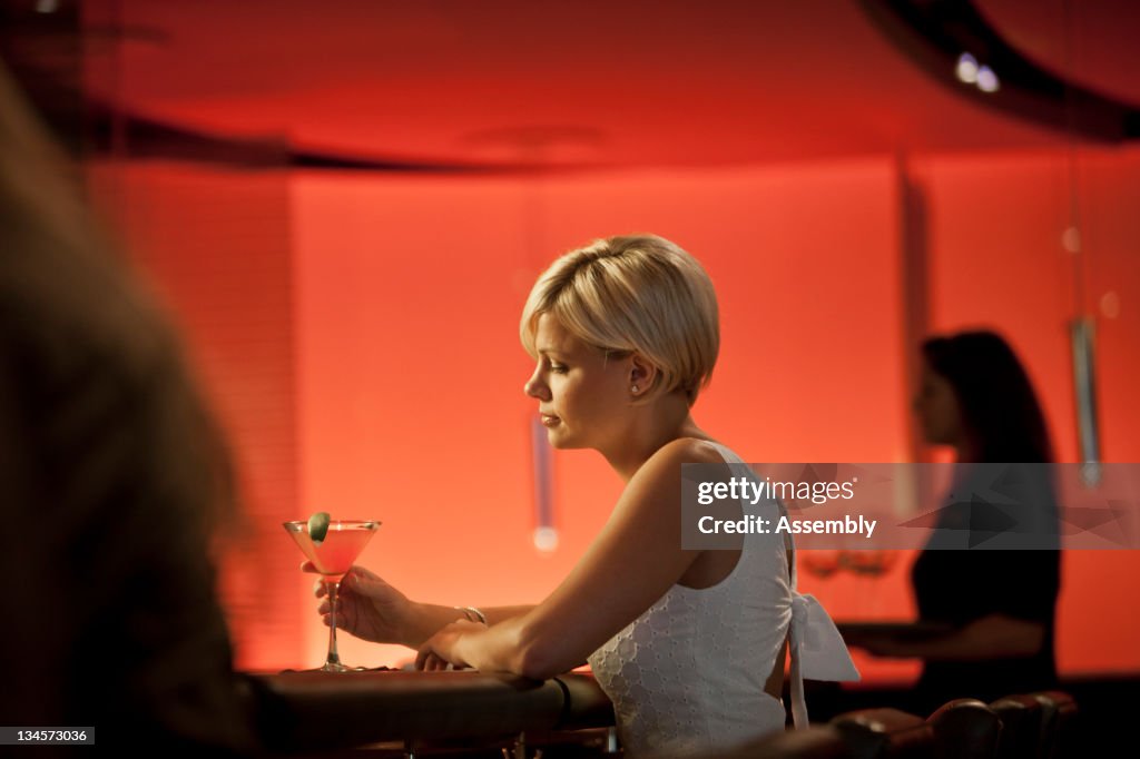 A young woman sits with her drink at a bar