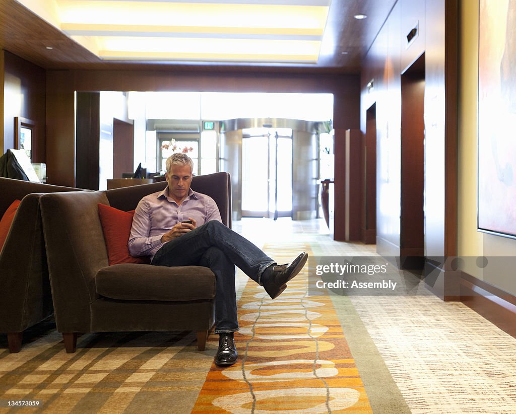 Mature man sitting in hotel lobby, texting.