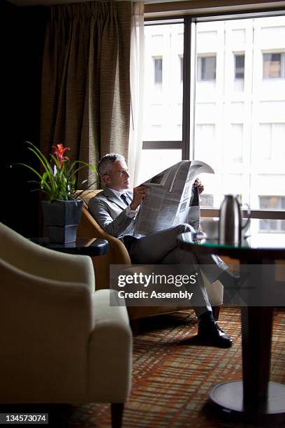 mature businessman reading newspaper in lounge - newspaper luxury stock-fotos und bilder