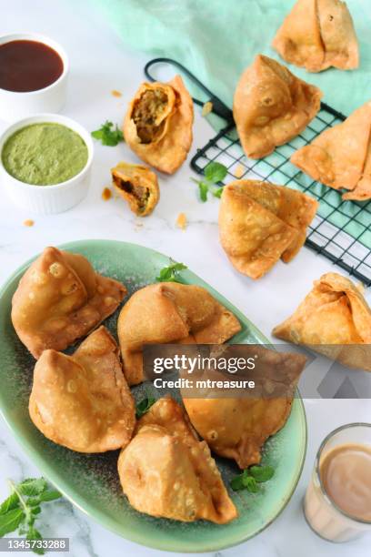 bild des grünen tellers mit gebratenen samosas, gefüllt mit gewürzten kartoffeln, erbsen und fleisch, kühlregal, grünem musselin, minzkorianderdip und mango-chutney-ramekins, glas chai-tee, marmoreffekthintergrund, erhöhte ansicht, fokus auf vordergr - rack focus stock-fotos und bilder