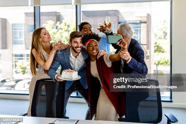 friendly multi-ethnic employees are celebrating birthday together and taking a selfie. - employee anniversary stock pictures, royalty-free photos & images