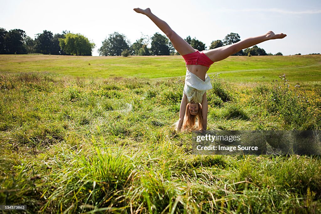 Young woman doing a handstand in a field