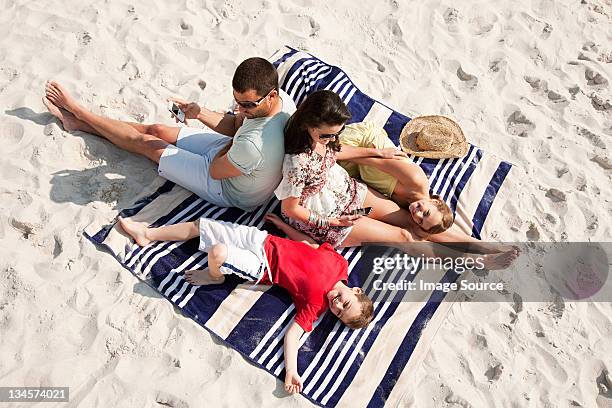 famiglia seduta e rilassarvi insieme su un tappeto su una spiaggia - telo da mare foto e immagini stock