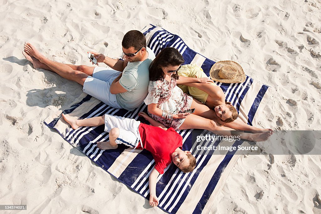 Family sitting and lying together on a rug on a beach