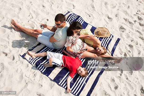 family sitting and lying together on a rug on a beach - sandy beach holiday stock pictures, royalty-free photos & images