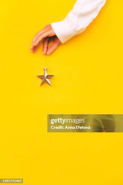 woman's hand is holding golden star on yellow background. concept of christmas preparation and decorating christmas tree. front view. trendy colors of the year - christmas background no people stock pictures, royalty-free photos & images