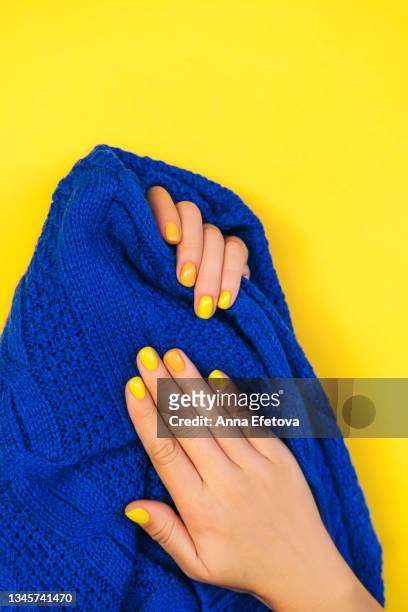 woman's hands with bright manicure are holding blue sweater on yellow background - touching fabric stock pictures, royalty-free photos & images