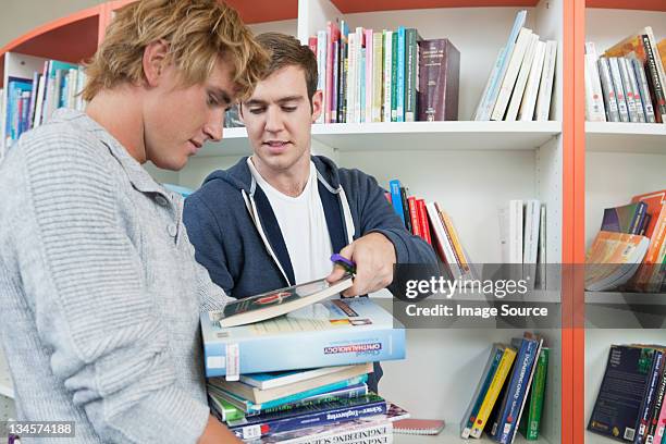 estudiantes universitarios elegir los libros de texto de la biblioteca - sólo hombres jóvenes fotografías e imágenes de stock