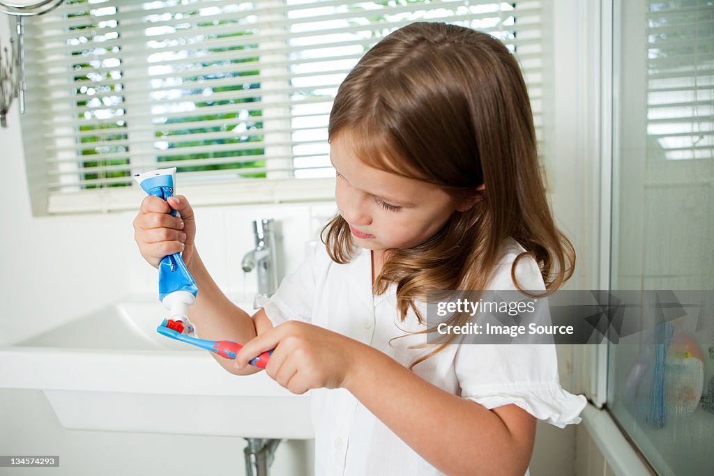 Girl applying toothpaste to brush in bathroom