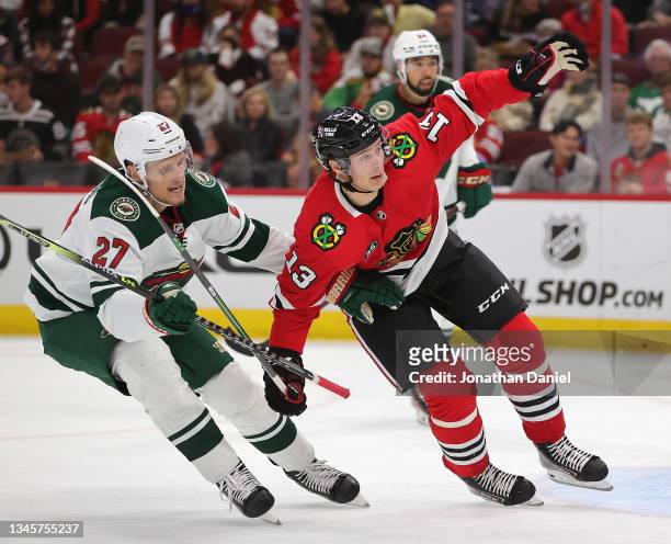 Nick Bjugstad of the Minnesota Wild and Henrik Borgstrom of the Chicago Blackhawks try to keep their balance as they battle for position during a...
