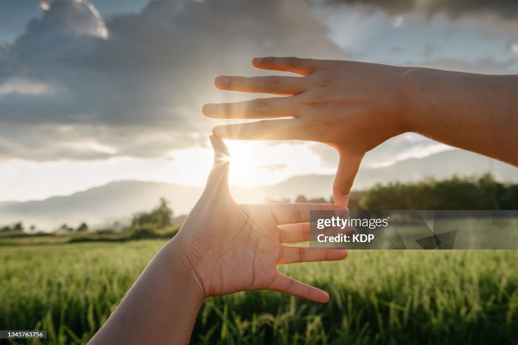Close-Up of Female Hand Outstretched Touching Scenic View Of Mountain Range During Sunset.