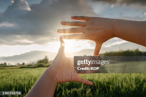 Close-Up of Female Hand Outstretched Touching Scenic View Of Mountain Range During Sunset. Close-Up of Female Hand Outstretched Touching Scenic View Of Mountain Range During Sunset.