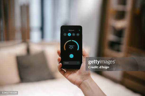 close up of woman's hand holding smartphone and setting up intelligent home system, remote-controlling the thermostat of smart air-conditioner in the living room of her smart home. smart living. lifestyle and technology - remote controlled fotografías e imágenes de stock