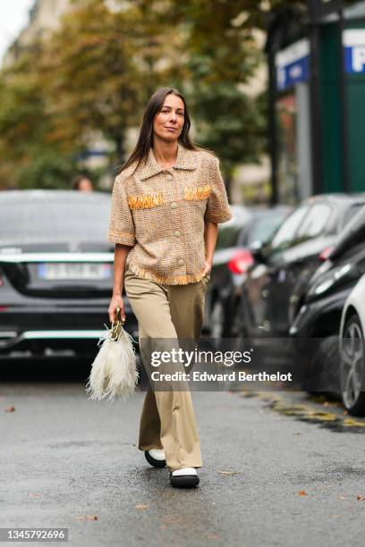 Alice Barbier wears silver earrings, a brown / orange / white checkered pattern in tweed short sleeves jacket, high waist beige brown flared pants, a...