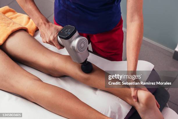 professional physiotherapist performs shock massage with a sports pistol on the stretcher in the medical office of the gym. concept of injury rehabilitation. close-up photography - percussion instrument stock pictures, royalty-free photos & images