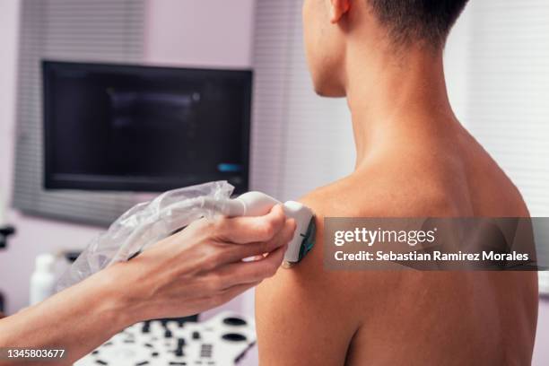 doctor using an ultrasound scanner on a shoulder of a young adult patient. - spalla foto e immagini stock
