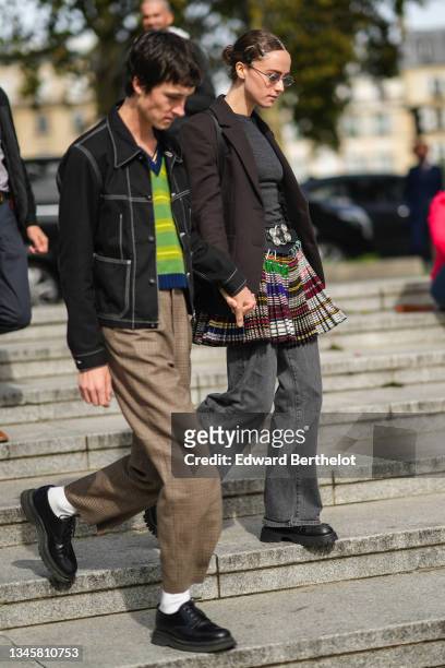 Sam Hine wears a green striped with navy blue V-neck pullover, a black denim with white seams buttoned jacket, brown with black and red checkered...
