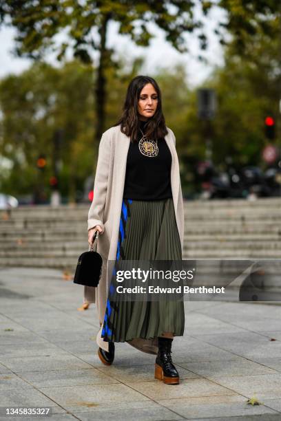 Guest wears a black high-neck pullover, a gold large pendant chain necklace, a beige long coat, a half khaki and half black and royal blue electric...