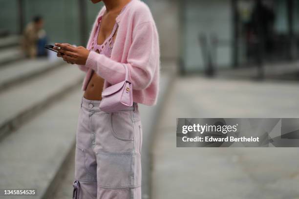 Guest wears a pale pink wool cardigan, a pale pink shiny leather crocodile pattern handbag, high waist denim cargo denim large pants, a pink...