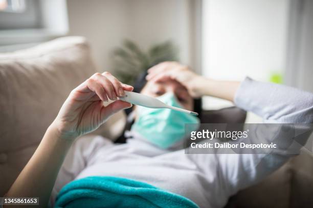 young woman is looking at the thermometer. she has fever. - pandemic illness stock-fotos und bilder