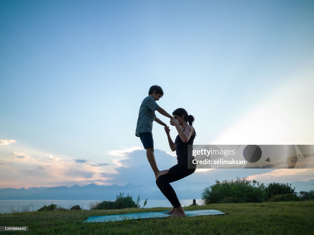 Photo Of Adult Woman And 8 Years Old Boy During Yoga Exercises In Sunset